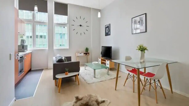 Una sala de estar moderna con una mesa de comedor de vidrio, un sofá, un televisor y un reloj en la pared.