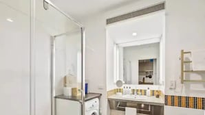 A compact bathroom with a glass shower enclosure, a washing machine, a sink with a mirror, and a towel rack. - Stylish Studio With Pool And Gym (Auckland)