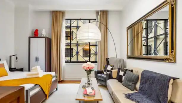 A modern hotel room with a bed, sofa, and a desk with a lamp. - Stylish Studio With Pool And Gym (Auckland)