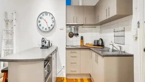 A compact kitchen with white cabinets, a clock, and basic appliances. - Stylish Studio With Pool And Gym (Auckland)