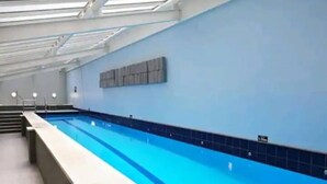 An indoor swimming pool with a long, narrow shape, tiled walls, and a clear blue water surface. - Stylish Studio With Pool And Gym (Auckland)