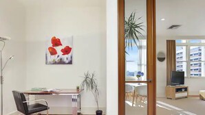 Un salon moderne avec un plancher en bois, un bureau avec une chaise, un téléviseur et une grande fenêtre donnant sur des immeubles.