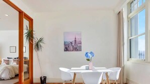 Un salon moderne avec un coin repas, un tableau représentant un paysage urbain et une grande fenêtre.