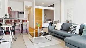 A modern living room with a grey sofa, a glass coffee table, and a dining area with chairs and a table.
