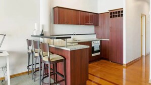 A compact kitchen with wooden cabinets, a built-in oven, and a small island with bar stools.