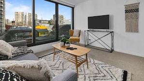 A modern living room with a large window, a sofa, a coffee table, and a TV on a stand. - Beautifully Modern Brand New Central Apartment (Auckland)
