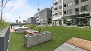 A modern building with a rooftop garden, concrete planters, and a view of a tower in the background. - Beautifully Modern Brand New Central Apartment (Auckland)