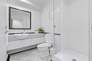 Une salle de bain moderne avec un lavabo, des toilettes et une douche, le tout de couleur blanche.