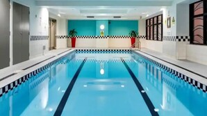 A swimming pool with a checkered pattern around the edges, a blue tiled floor, and a teal-colored wall with a warning sign.