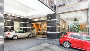 A hotel entrance with a glass facade, a Christmas tree, and two cars parked in front.