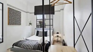 Ein modernes Schlafzimmer mit einem Bett, einem Holztisch, einem Kleiderständer und einem Wandbild mit Muster.