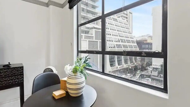 Ein Zimmer mit einem großen Fenster, einem runden Tisch mit einer Vase und einer Pflanze sowie einem Stuhl.
