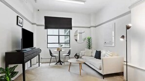 Ein modernes Wohnzimmer mit Flachbildfernseher, einer Couch, einem Couchtisch und einem Essbereich mit Stühlen.