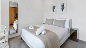 Une chambre d’hôtel moderne avec un grand lit, une table de chevet, une chaise et un miroir.