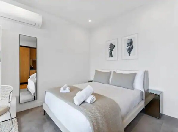 Una habitación de hotel moderna con una cama grande, una mesita de noche, una silla y un espejo.