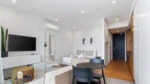 Un salon moderne et bien éclairé, équipé d’un téléviseur à écran plat, d’un canapé, d’une table à manger avec des chaises et d’une petite table d’appoint.