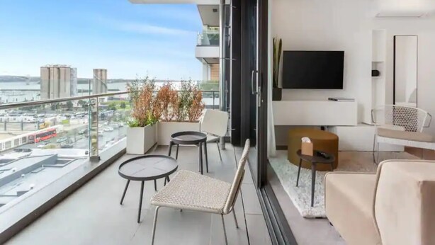 Un balcon moderne offrant une vue sur la ville, une télévision à écran plat et un coin salon avec un canapé et des fauteuils.