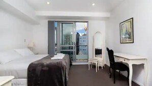 Ein Hotelzimmer mit einem Bett, einem Schreibtisch, einem Sessel und einem großen Fenster mit Blick auf Gebäude.