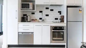 Een moderne keuken met witte kasten, een magnetron, een koffiezetapparaat, een waterkoker, een koelkast en een oven.