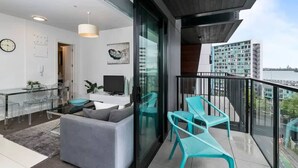 Een modern appartement met balkon, een woonruimte met een bank en televisie, en uitzicht op de stad.
