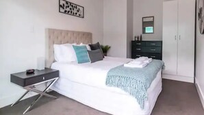 Een slaapkamer met een bed, nachtkastje, kledingkast en een kunstwerk aan de muur.