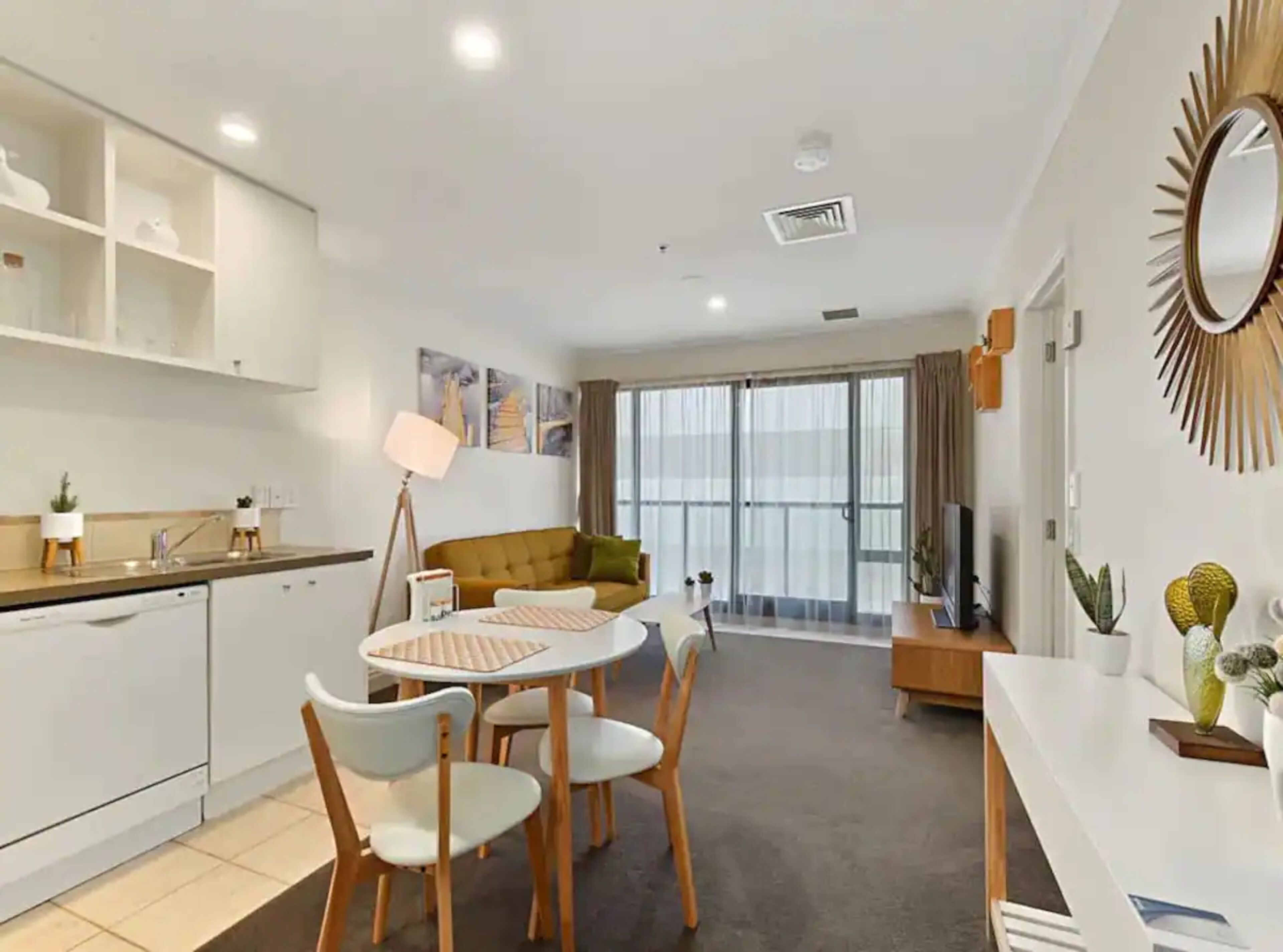A modern living room with a sofa, a dining table with chairs, and a kitchen area with cabinets and a sink.