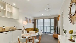 A modern living room with a sofa, a dining table with chairs, and a kitchen area with cabinets and a sink. - Pool, Gym And Style In The Cbd (Auckland)