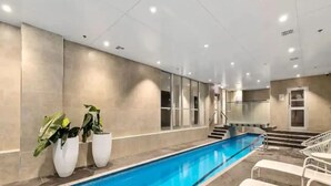 An indoor swimming pool with clear blue water, surrounded by tiled walls and a staircase leading to an upper level. - Stylish Central City 1-Bedroom With Patio (Auckland)