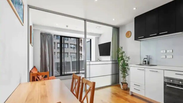 A modern kitchen with a dining area, a large window, and a view of the city. - Stylish Central City 1-Bedroom With Patio (Auckland)