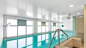 An indoor swimming pool with clear glass walls, a metal ladder, and a tiled floor.