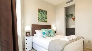 A bedroom with a bed, a nightstand, a wardrobe, and a painting on the wall. - Lovely Apartment - Gym & Parking by Zodiak Stays (Auckland)