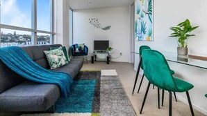 A modern living room with a sofa, a TV, and a green chair. - Lovely Apartment - Gym & Parking by Zodiak Stays (Auckland)
