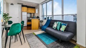 A modern apartment with a kitchen, dining area, and a large window with a city view. - Lovely Apartment - Gym & Parking by Zodiak Stays (Auckland)