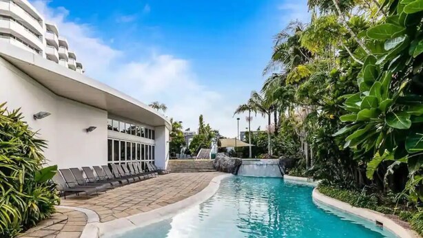 A swimming pool with lounge chairs, a modern building, and tropical vegetation. - Lovely Apartment - Gym & Parking by Zodiak Stays (Auckland)