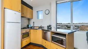 A modern kitchen with wooden cabinets, a built-in oven, a microwave, and a large window offering a city view. - Lovely Apartment - Gym & Parking by Zodiak Stays (Auckland)