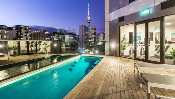 A rooftop pool with a city skyline view, including a tall tower with a spire. - Condo in Queen St CBD w Pool and Gym Zodiak Stays (Auckland)