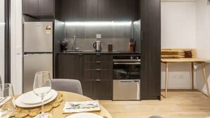 A compact kitchen with dark cabinetry, a stainless steel refrigerator, a built-in oven, and a dishwasher. - Condo in Queen St CBD w Pool and Gym Zodiak Stays (Auckland)