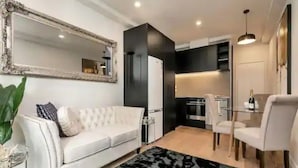 Een moderne woonkamer met een witte bank, een zwart-wit vloerkleed, een grote spiegel en een eethoek met een glazen tafel en stoelen.