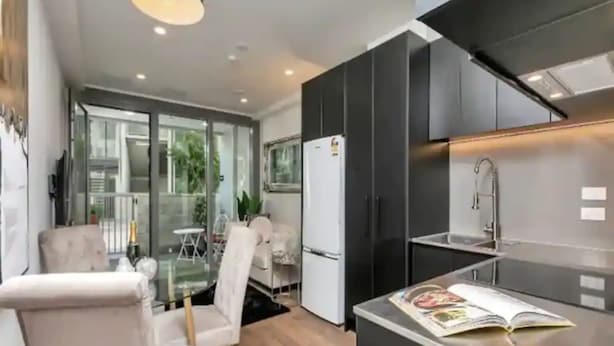 Een moderne keuken met donkere kastjes, een ingebouwde oven en een glazen eethoek met een witte tafel en stoelen.