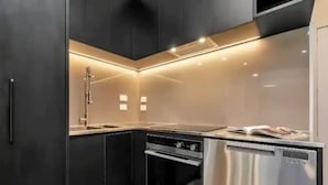 Een moderne keuken met donkere kastjes, roestvrijstalen apparatuur en verlichting onder de kast.