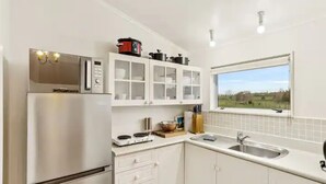 A modern kitchen with white cabinets, a built-in microwave, a stove, and a window with a view of the countryside. - Charming 3 Bedroom Home In Tranquil Rural Karaka (Karaka)