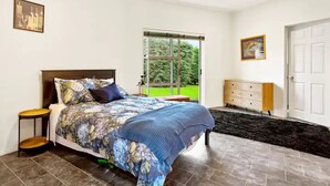A bedroom with a bed, a nightstand, a dresser, a window, and a door. - Charming 3 Bedroom Home In Tranquil Rural Karaka (Karaka)