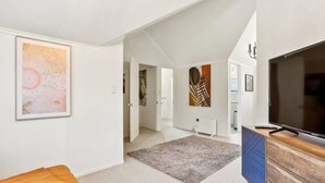 A spacious living room with a large TV, a blue cabinet, and artwork on the walls. - Charming 3 Bedroom Home In Tranquil Rural Karaka (Karaka)