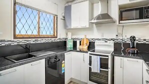 A kitchen with white cabinets, a black countertop, a microwave, an oven, and a window with a metal screen.