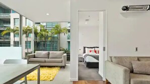Uma sala de estar moderna com sofá, mesa de jantar e vista para um quarto com cama e mesa de cabeceira.