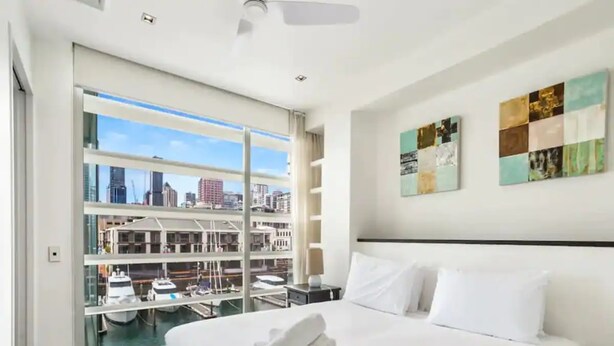 Een hotelkamer met een groot bed, uitzicht op een jachthaven en een stadsgezicht door middel van ramen van de vloer tot aan het plafond.