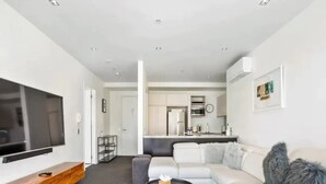 Een moderne woonkamer met een flatscreen televisie, een houten tv-meubel, een grijze bank en een ronde salontafel.