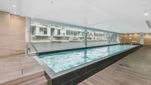 Zwembad met glazen omheining, houten terras en een modern interieur.