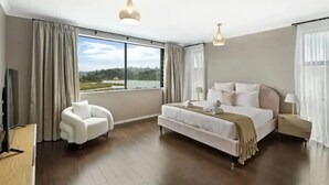 A modern hotel room with a large bed, a sofa, a TV, and a view of a lake. - North Shore Mansion With 20M Pool (Auckland)