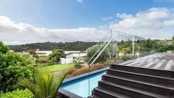 A pool area with steps leading down to the water, surrounded by greenery and a clear sky.